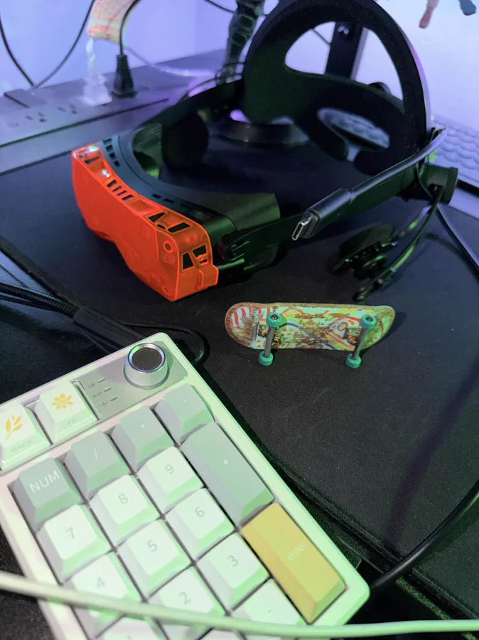 An orange Beyond 2 on a desk with a racing wheel and a green mechanical keyboard