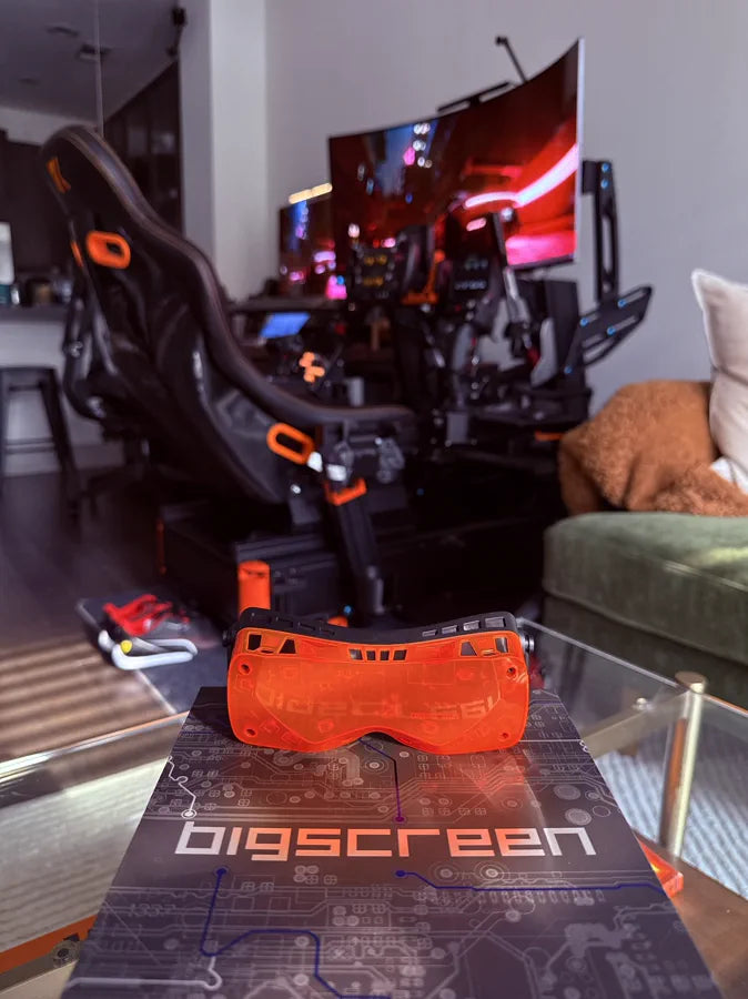 An orange Beyond 2 on a Bigscreen desk mat in front of a lit sim rig